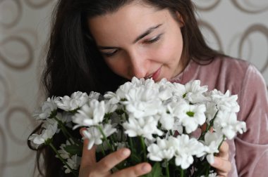 Kız bir buket beyaz çiçeği kokluyor. Esmer, sevgilisinden bir buket narin çiçeği kokluyor. Sevgili yarın için güzel bir hediye..