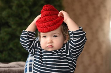 Bir çocuk şapka takıyor. Kırmızı bir şapka ve bir çocuk. Parmağını gösteriyor. Çocuk 0-1 yaşlarında. bir yıllık çocuk portresi.