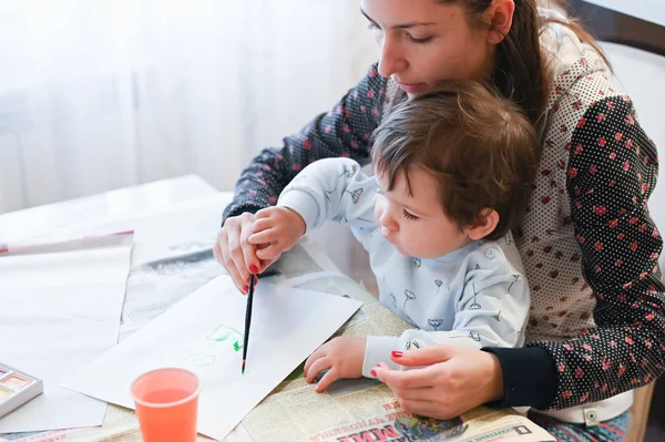 A child draws on his mothers lap. The child sits on his lap with his mother and draws gouache. Dusseldorf, Germany - October 11, 2019.