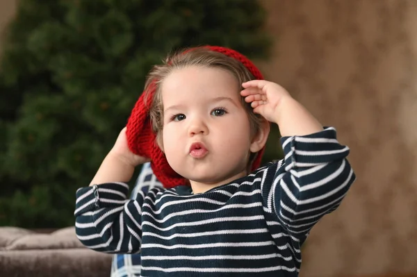 Ett barn sätter på sig en hatt. En röd hatt och ett barn. visar ett finger. Barnet är 0-1 år. ett år gammalt barnporträtt. — Stockfoto