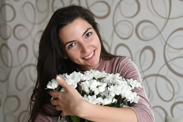 Menina abraça um buquê de flores brancas. Abraços morena cheira um buquê de flores delicadas de sua amada. Um bom presente para sua metade amada . — Fotografia de Stock