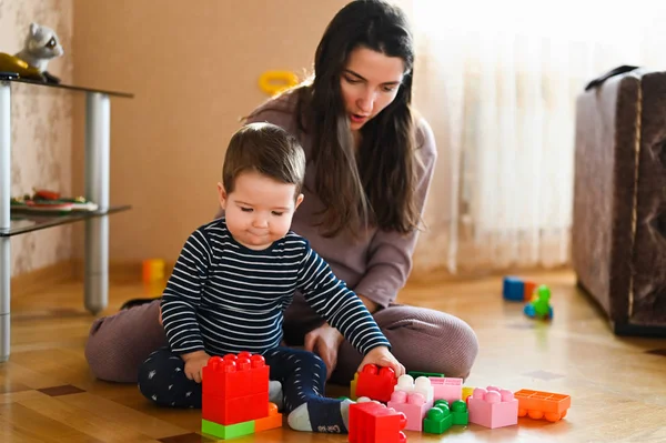 Mamma och barnet leker på golvet. Vackra barn leker med leksaker med lycklig mor inomhus — Stockfoto