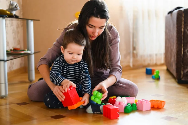 Mamma och barnet leker på golvet. Vackra barn leker med leksaker med lycklig mor inomhus — Stockfoto