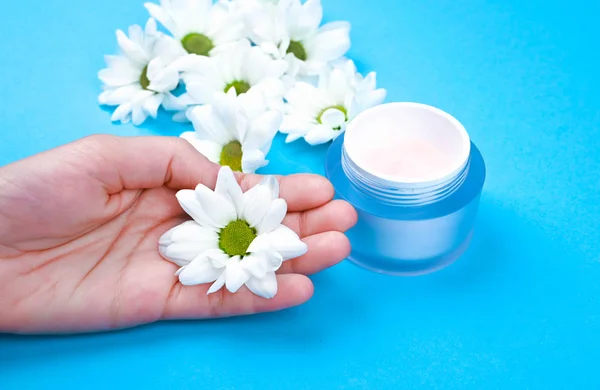 hands with flowers with a jar of cream on a blue background. View from above. Natural cosmetic. place to record.