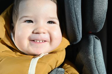 Bebek çocuk araba koltuğunda gülümsüyor. Güneş yüzünüzde parlıyor. Yakın plan.