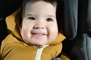 Bebek çocuk araba koltuğunda gülümsüyor. Güneş yüzünüzde parlıyor. Yakın plan.
