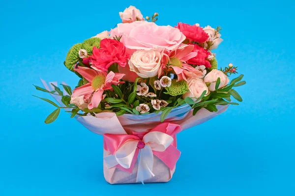 Bouquet of flowers in pink packaging on a blue background. Congratulations to the women. Flowers are favorite