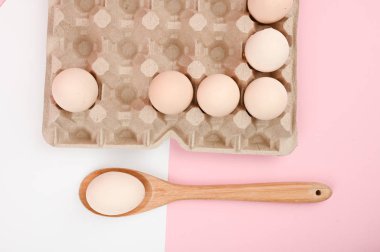 Tahta kaşıkta yumurta. Beyaz ve pembe arka planda bir tepsi yumurta. Testisli eko tepsisi. Minimalist trend, üst görüş. Yumurta tepsisi. Paskalya konsepti