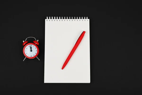 黒の背景に鉛筆と赤の目覚まし時計とオープンノートブックの上のトップビューデスク — ストック写真