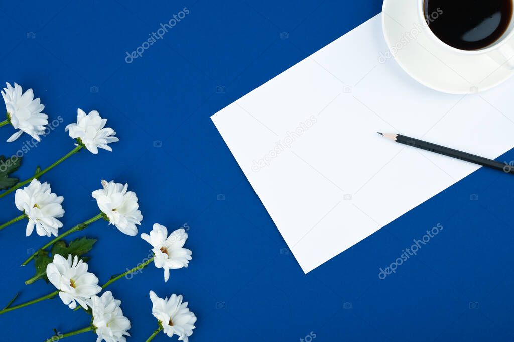 Female workspace. A cup of coffe and flowers frame on blue background. Copy space.