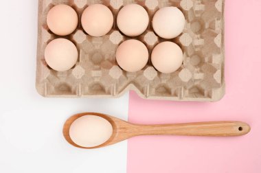 Tahta kaşıkta yumurta. Beyaz ve pembe arka planda bir tepsi yumurta. Testisli eko tepsisi. Minimalist trend, üst görüş. Yumurta tepsisi. Paskalya konsepti
