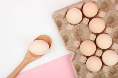 Tahta kaşıkta yumurta. Beyaz ve pembe arka planda bir tepsi yumurta. Testisli eko tepsisi. Minimalist trend, üst görüş. Yumurta tepsisi. Paskalya konsepti