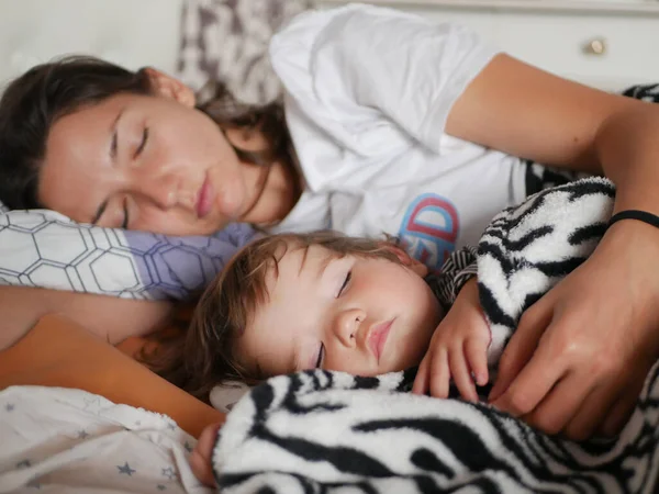 Sleeping mother hugged a sleeping baby. Mother and her little son sleep in a large bed, hiding in a blanket