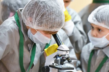 Mikroskop ve çocuklar. Tıp önlüklü çocuklar mikroskopla bakıyorlar. Tıp öğretiyorum. Hastanedeki bir seminerde genç doktorlar. KHARKIV, UKRAINE - 20 HAZİRAN 2020.