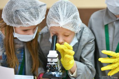 Mikroskop ve çocuklar. Tıp önlüklü çocuklar mikroskopla bakıyorlar. Tıp öğretiyorum. Hastanedeki bir seminerde genç doktorlar. KHARKIV, UKRAINE - 20 HAZİRAN 2020.