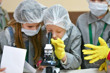 Mikroskop ve çocuklar. Tıp önlüklü çocuklar mikroskopla bakıyorlar. Tıp öğretiyorum. Hastanedeki bir seminerde genç doktorlar. KHARKIV, UKRAINE - 20 HAZİRAN 2020.