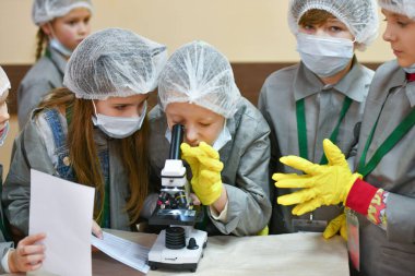 Mikroskop ve çocuklar. Tıp önlüklü çocuklar mikroskopla bakıyorlar. Tıp öğretiyorum. Hastanedeki bir seminerde genç doktorlar. KHARKIV, UKRAINE - 20 HAZİRAN 2020.