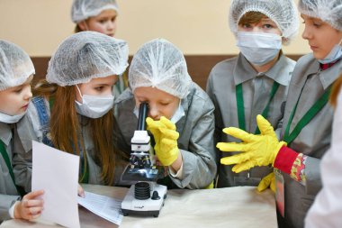 Mikroskop ve çocuklar. Tıp önlüklü çocuklar mikroskopla bakıyorlar. Tıp öğretiyorum. Hastanedeki bir seminerde genç doktorlar. KHARKIV, UKRAINE - 20 HAZİRAN 2020.