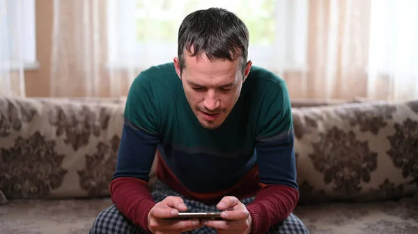 A man sits on a sofa and plays on the phone at home.