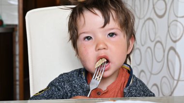 Çocuk masada çatalla makarna yiyor..