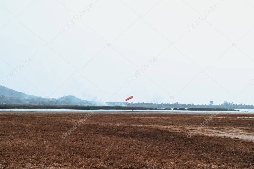 Red wind sock beside runways on small airfield. brown dried grasses in foreground and smoke in background.