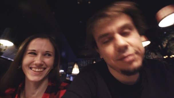 Молодая привлекательная пара веселится в кафе, делая смешные лица в камеру — стоковое видео