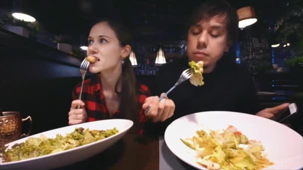 Joven pareja atractiva está cenando en la cafetería, comiendo ensaladas, hablando — Vídeo de stock