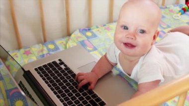 Gülümseyen ve yatağının içinde laptop oynamaktan 6 aylık erkek bebek portresi