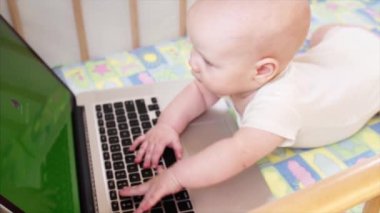 6 aylık bebek yatağının içinde laptop ile oynarken yavaş portresi