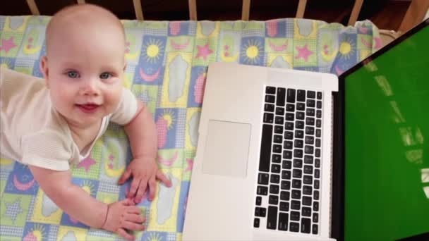 Retrato del niño que sonríe a alguien y está acostado en su cama cerca de la computadora portátil — Vídeo de stock