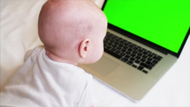 6 months old baby boy is lying on bed in front of laptop with chroma key screen — Stock Video