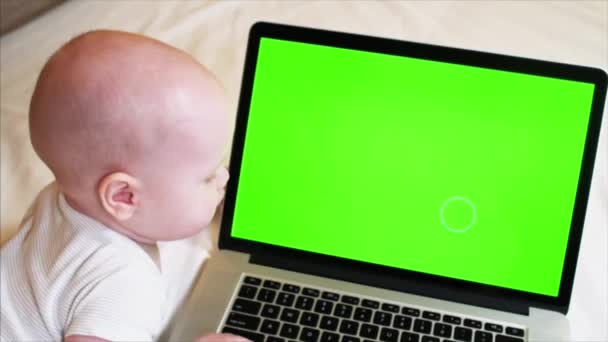 6 months old baby boy is lying on bed in front of laptop with chroma key screen — Stock Video