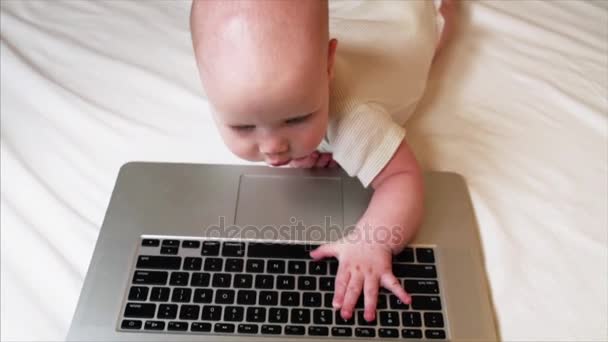 Retrato de adorable bebé de 6 meses acostado en la cama y jugando con el ordenador portátil — Vídeo de stock