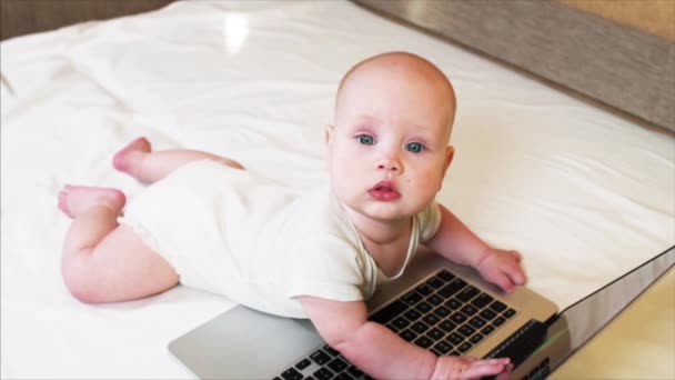 Bébé garçon est couché sur un lit devant l'ordinateur portable et regardant quelqu'un — Video