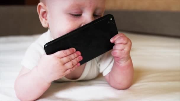 正在咀嚼和吸吮黑色智能手机的男婴的肖像 — 图库视频影像
