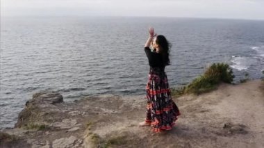 Okyanusun üzerindeki yüksek uçurumda dans eden güzel elbiseli çingene kadının hava panoramik görüntüsü.
