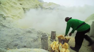 JAVA, INDONESIA - JULY 7, 2019: Indonesian man without respirator loading toxic sulphur into backets without equipment surrounded by poisonous fumes of Ijen volcano 