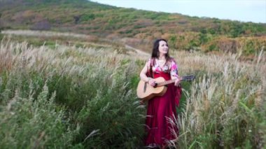 Uzun elbiseli güzel çingene kadın. Gitar çalıyor ve otların arasında şarkı söylüyor.
