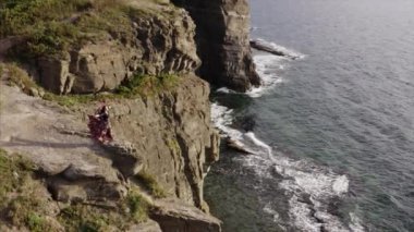 Okyanusun yukarısındaki yüksek kayalıklarda duran güzel elbiseli çingene kadının hava panoramik görüntüsü.