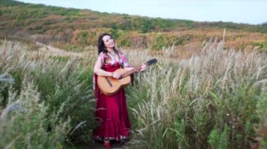 Uzun elbiseli güzel çingene kadın. Gitar çalıyor ve otların arasında şarkı söylüyor.
