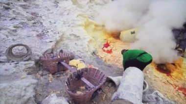 JAVA, INDONESIA - JULY 7, 2019: Indonesian man without respirator throwing toxic sulphur into baskets without equipment  surrounded by poisonous fumes of Ijen volcano 