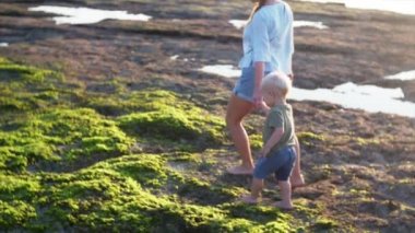 Kafkasyalı anne ve iki yaşındaki çocuk sular çekildiğinde ıslak taşların üzerinde yürüyor akşam güneşinin, Balangan sahilinin, Bali 'nin, Endonezya' nın tadını çıkarıyor.
