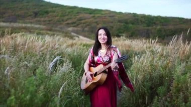Uzun elbiseli güzel çingene kadın çayırlarda dans ederken gitar çalıyor ve şarkı söylüyor.