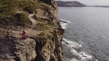 Okyanusun üzerindeki yüksek uçurumda dans eden güzel elbiseli çingene kadının hava panoramik görüntüsü.