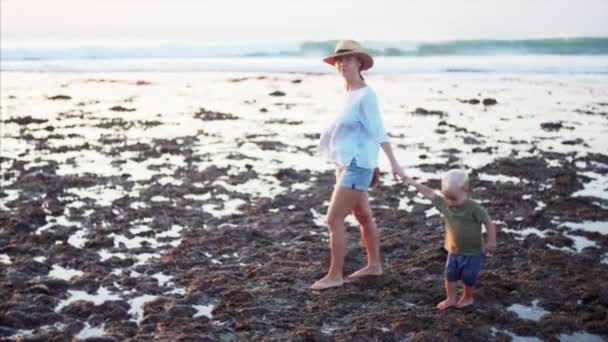 白人の母親と2歳の男の子が干潮時にぬれた石の上を歩いて夜の太陽 Balanganビーチ インドネシア — ストック動画