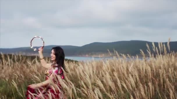 在蓝天背景的田野里 一个身穿漂亮衣服 头晕目眩的女人与手鼓共舞的景象 — 图库视频影像