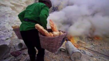 JAVA, INDONESIA - JULY 7, 2019: Indonesian man carrying extremely heavy baskets with sulphur surrounded by poisonous fumes of Ijen volcano 