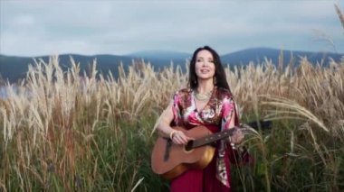 Uzun elbiseli güzel çingene kadın. Gitar çalıyor ve otların arasında şarkı söylüyor.