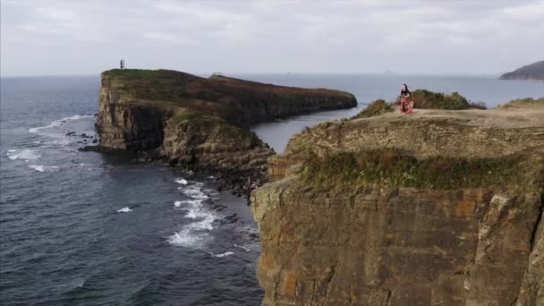 空中全景 身穿漂亮衣服 身披长袍 在高高的悬崖上行走在海面上的女人 — 图库视频影像