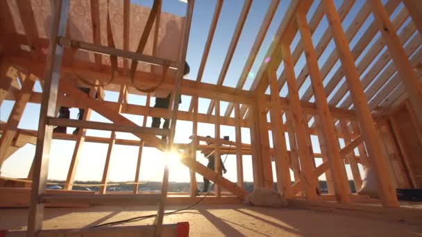 View of builders covering roof with waterproofing layer at unfinished frame house interior with wooden beams of roof and walls with blue sky on background — Stock Footage View Builders Covering Roof Waterproofing Layer Unfinished Frame House Interior Stock Footage